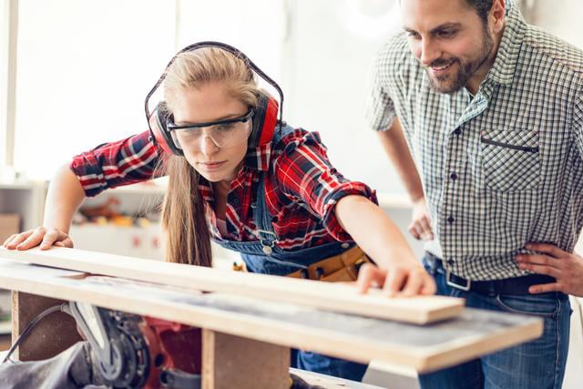 Jeune femme apprentie en train de travaille les métiers du bois avec son maître d'apprentissage.